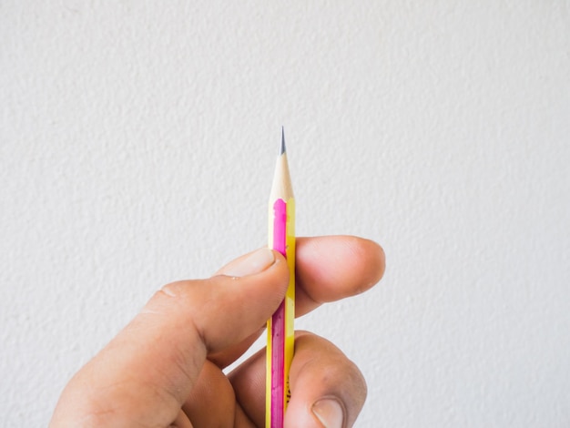 Foto primer plano de una mano sosteniendo un lápiz contra la pared