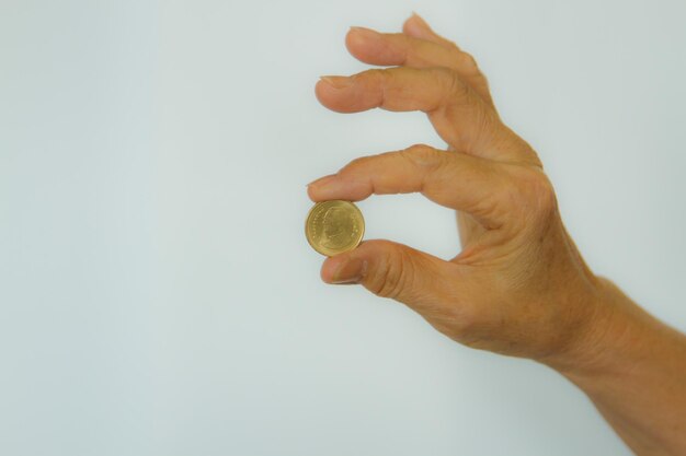 Primer plano de la mano sosteniendo una moneda contra un fondo blanco