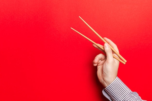 Foto primer plano de la mano sosteniendo palillos contra un fondo de color