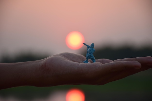 Foto primer plano de una mano sosteniendo un pequeño juguete contra el cielo durante la puesta de sol