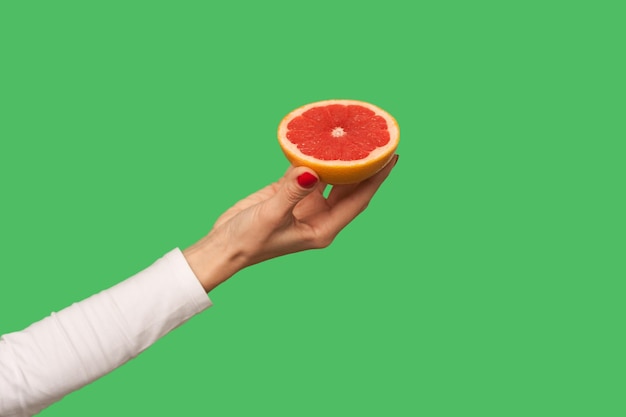 Primer plano de la mano sosteniendo pomelo jugoso en rodajas, fruta sabrosa para la desintoxicación, comida vegetariana orgánica natural llena de vitaminas, dieta saludable y concepto de pérdida de peso. interior, aislado sobre fondo verde