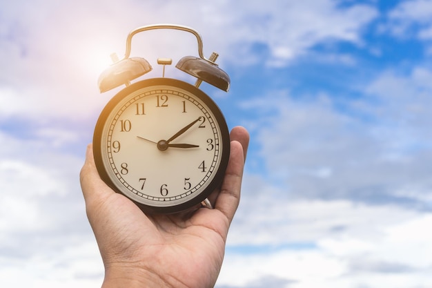 Foto primer plano de la mano sosteniendo el reloj contra el cielo