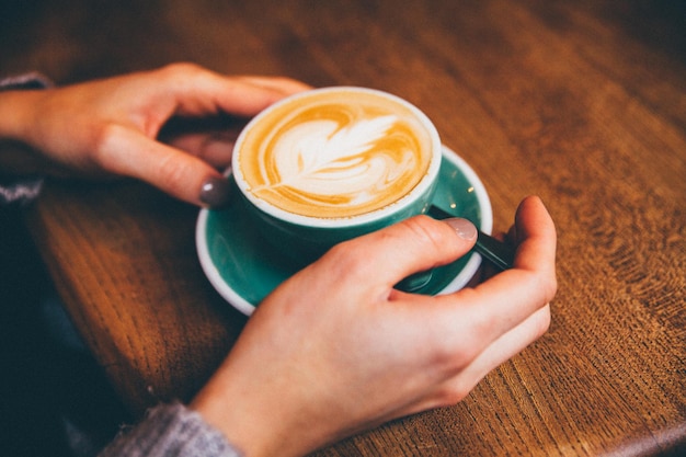 Primer plano de una mano sosteniendo una taza de café en la mesa