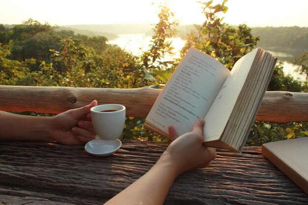 Foto primer plano de una mano sosteniendo una taza de café y una novela en la mesa