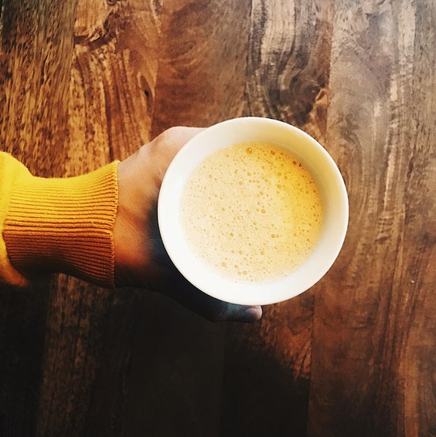 Primer plano de una mano sosteniendo una taza de té en la mesa