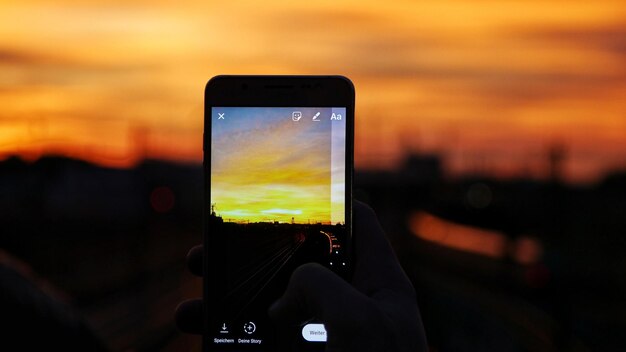 Foto primer plano de la mano sosteniendo el teléfono inteligente contra la puesta de sol