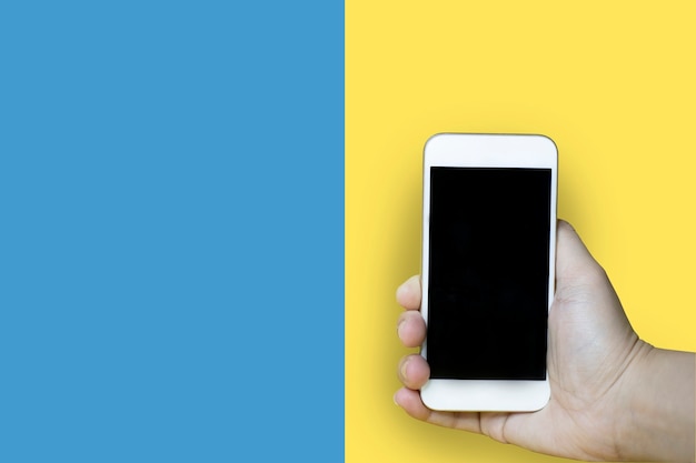 Primer plano de una mano sosteniendo un teléfono móvil con un fondo azul-amarillo, utilizado para fotos publicitarias, trazado de recorte.