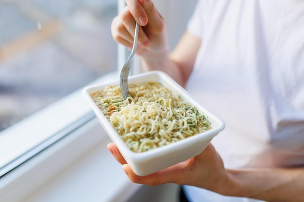 Un primer plano de una mano sosteniendo un tenedor en un plato de fideos instantáneos