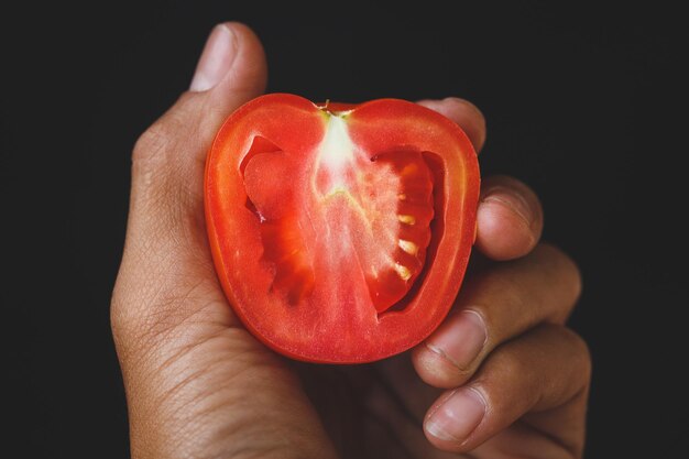 Primer plano de la mano sosteniendo un tomate contra un fondo negro