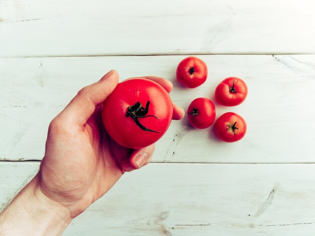 Foto primer plano de la mano sosteniendo un tomate sobre la mesa