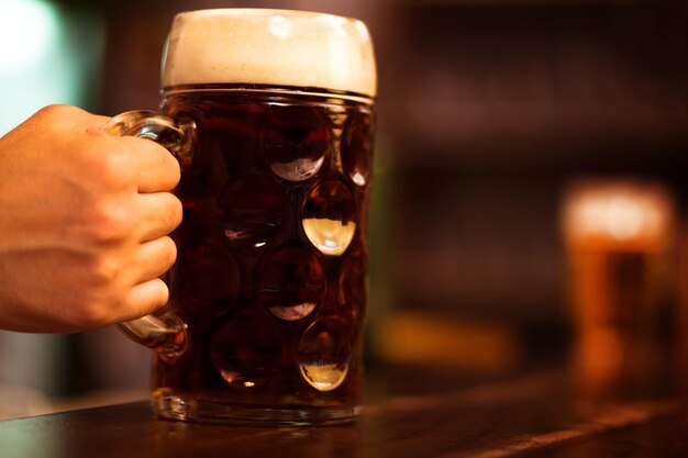 Foto primer plano de una mano sosteniendo un vaso de cerveza en la mesa