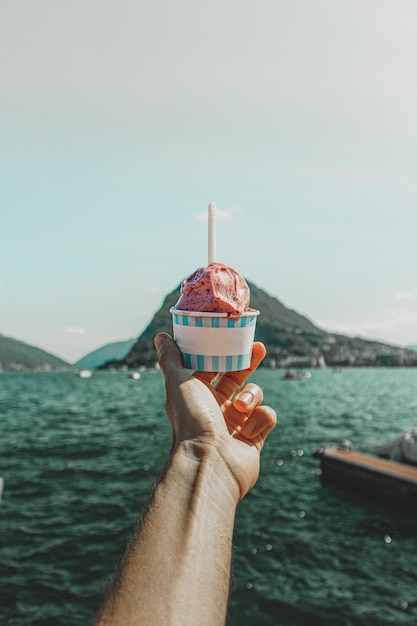 Primer plano de una mano sujetando una copa de helado contra el paisaje del lago