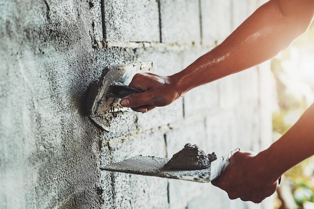 Primer plano de la mano del trabajador de enlucido de cemento en la pared para la construcción de la casa