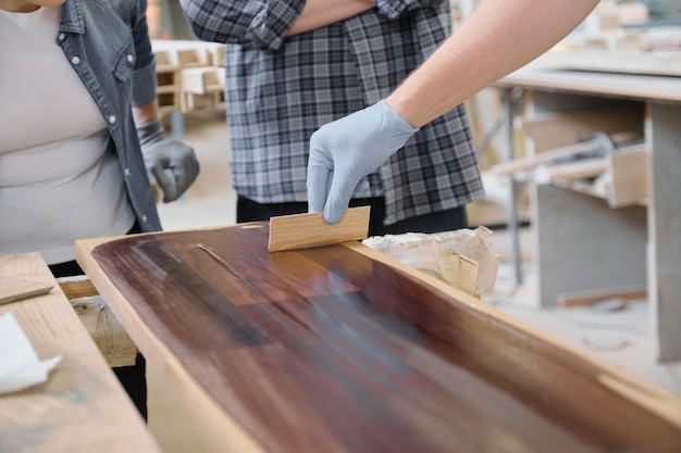 Primer plano de la mano de los trabajadores que cubre el tablón de madera con acabado de cubierta protectora para madera