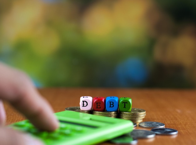 Foto primer plano de la mano usando una calculadora por texto hecho con bloques de juguete sobre monedas en la mesa