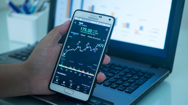 Primer plano de la mano usando un teléfono móvil con una computadora portátil