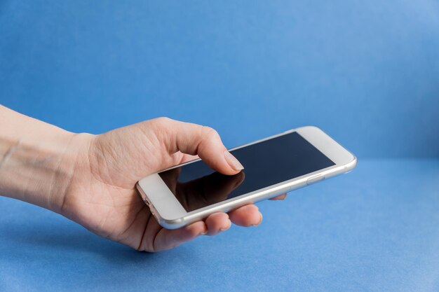 Primer plano de la mano usando un teléfono móvil contra un fondo azul