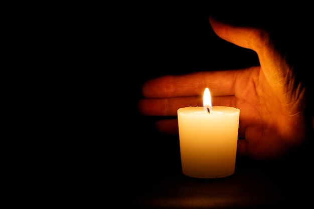 Primer plano de la mano con una vela encendida contra un fondo negro