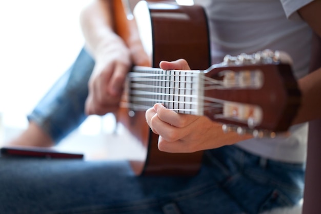 Primer plano de manos adolescente tocando la guitarra acústica. Tener un hobby. Chico relajante tocando la guitarra. Enfoque suave.