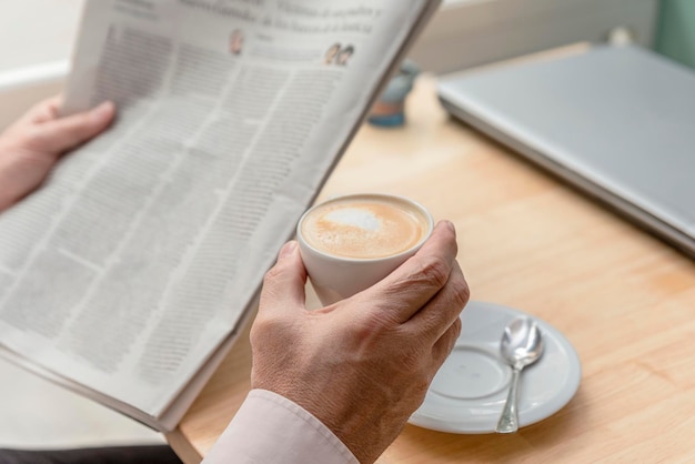 Primer plano de las manos de un anciano irreconocible sosteniendo un periódico en la mano y una taza de café