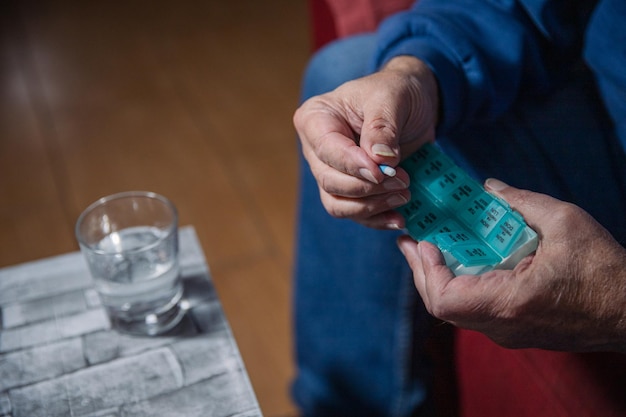 Primer plano de las manos de un anciano tomando medicamentos de su dispensador de medicamentos