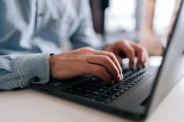 Primer plano de las manos arrugadas de un hombre de negocios mayor irreconocible escribiendo en el teclado de una computadora portátil