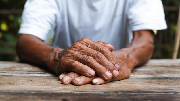 Primer plano de las manos arrugadas masculinas que el anciano lleva puesto en la mesa de madera