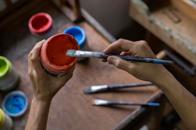 Primer plano de las manos de una artista latinoamericana irreconocible colocando pintura en un pincel mientras pinta cuadros en un estudio de arte Concepto de artista y hobby