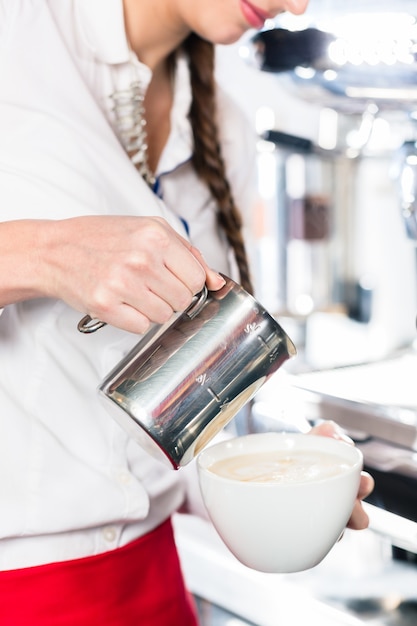 Primer plano de las manos de una camarera vertiendo leche en una taza de café