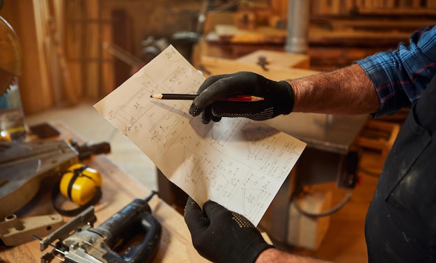 Primer plano de manos de carpintero con planes de planos para hacer un mueble en el taller de carpintería