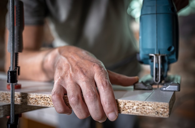 Primer plano de las manos de un carpintero en el proceso de corte de madera con una sierra de calar.