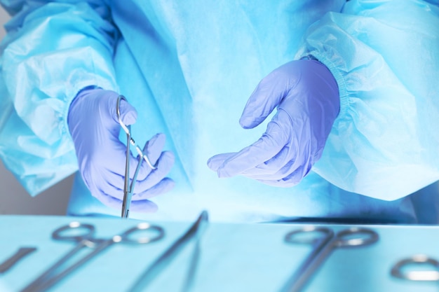 Primer plano de las manos de los cirujanos en el trabajo en el quirófano en tonos azules. Equipo médico realizando operación