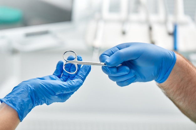 Primer plano de las manos de un dentista y un enfermero cirujano en un quirófano durante una operación de implante dental