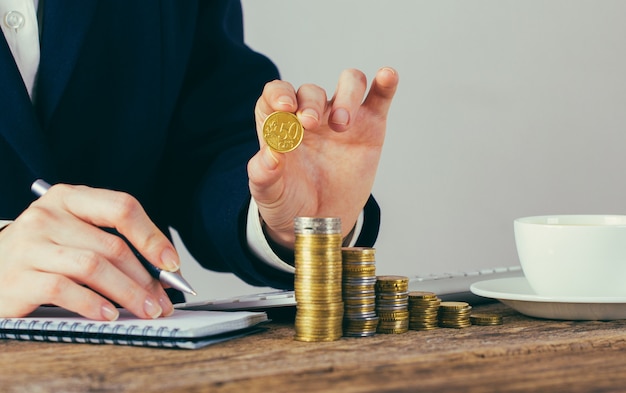 Primer plano de las manos de la empresaria con monedas de dinero en la oficina en el escritorio de madera