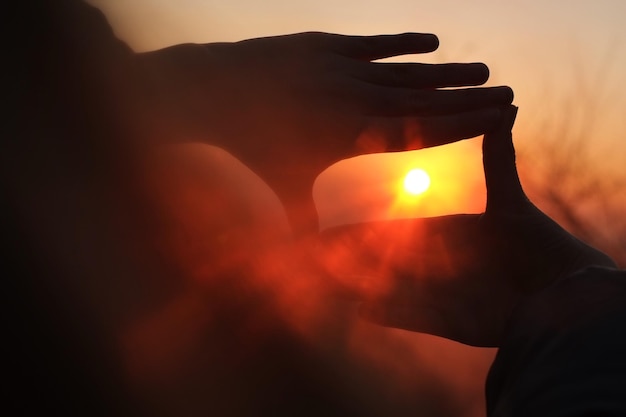 Primer plano de las manos enmarcando el sol al atardecer
