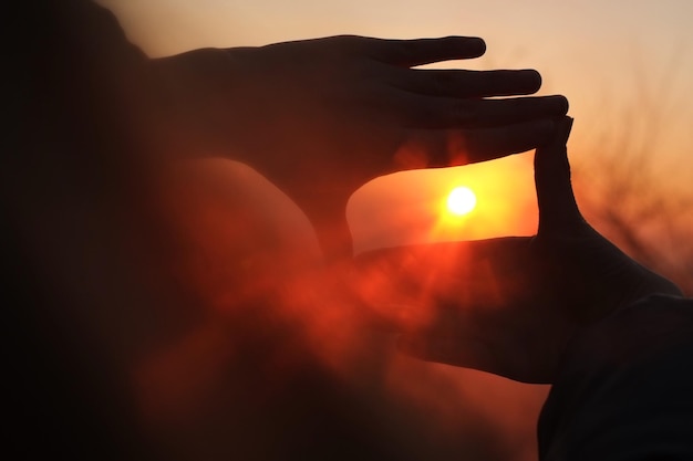 Foto primer plano de las manos enmarcando el sol al atardecer