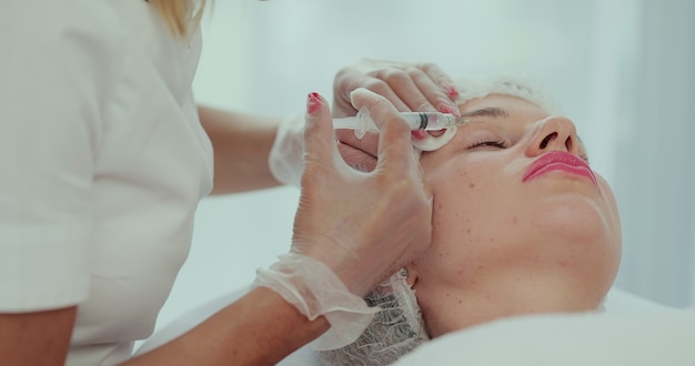Primer plano de las manos de la esteticista haciendo inyección de elevación de la piel facial a la cara de la mujer joven. Paciente de sexo femenino hermoso que recibe el procedimiento de la belleza. Tratamiento cosmético.