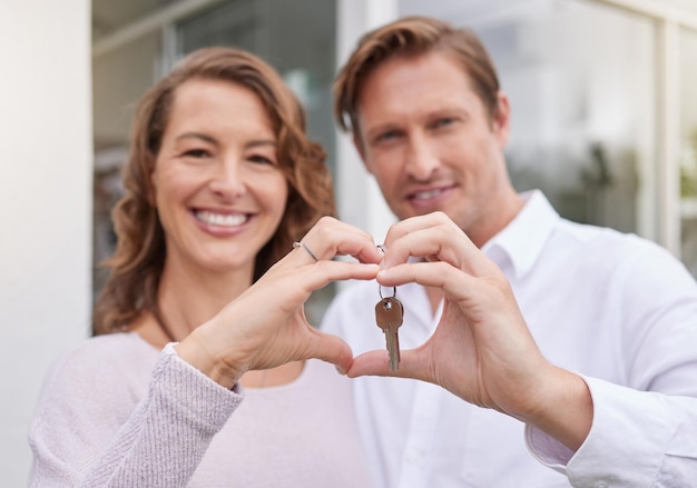 Primer plano de las manos de la feliz pareja casada sosteniendo las llaves de la nueva casa con un gesto de mano en forma de corazón Hombre y mujer sosteniendo las llaves de la nueva casa o apartamento