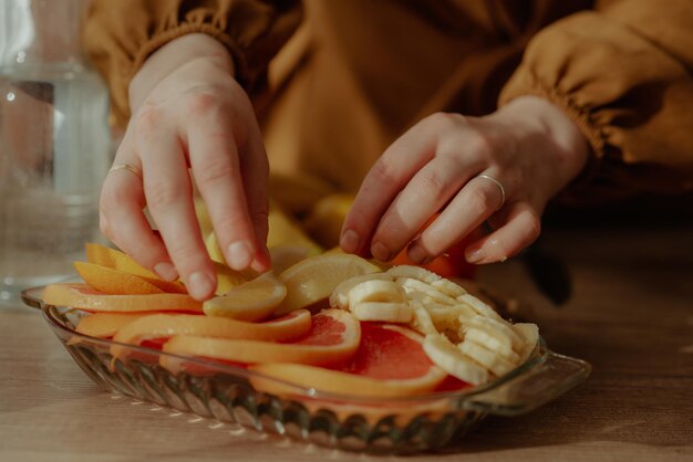 Un primer plano de manos femeninas arreglando deliciosas rebanadas de pomelo, plátano y limón en un plato