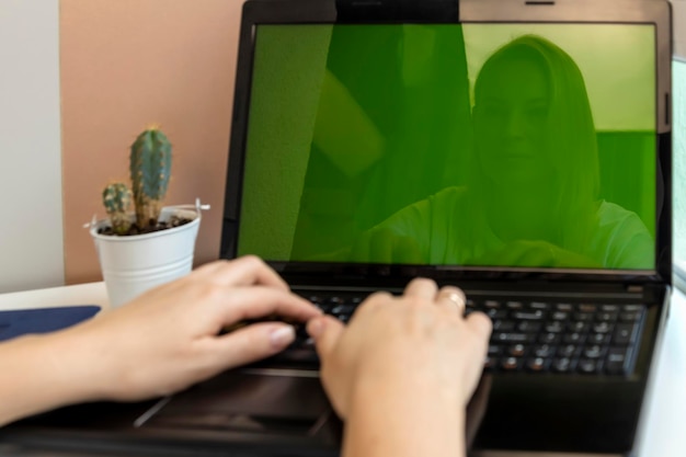 Primer plano de manos femeninas en la computadora portátil con pantalla verde Imagen de una niña en la pantalla de una computadora Centrarse en la cara de la niña