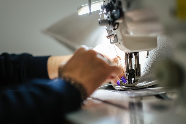 Primer plano de manos femeninas cosiendo cuero gris en una máquina