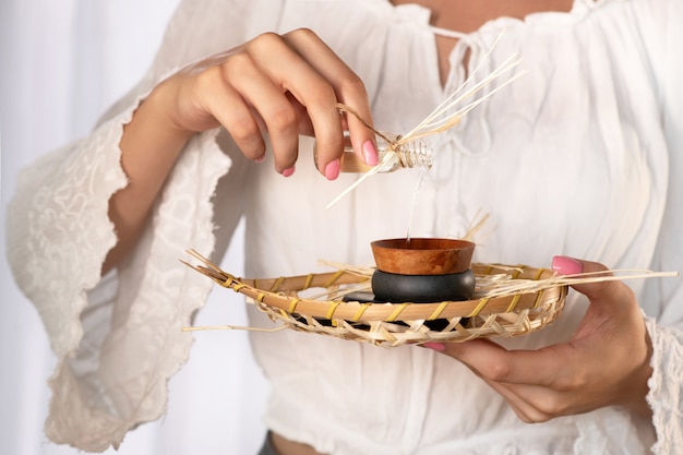 PRIMER PLANO: manos femeninas con delicada manicura rosa vierten aceite en un platillo para hacer un masaje. Masaje tailandés con piedras. SPA Y CUIDADO