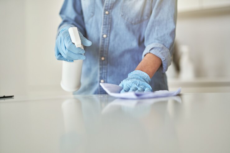 Foto primer plano de manos femeninas en guantes de goma con detergente en aerosol y paño durante la limpieza