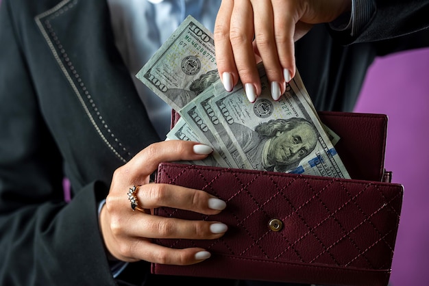 Primer plano de manos femeninas poniendo un billete de un dólar en su bolso