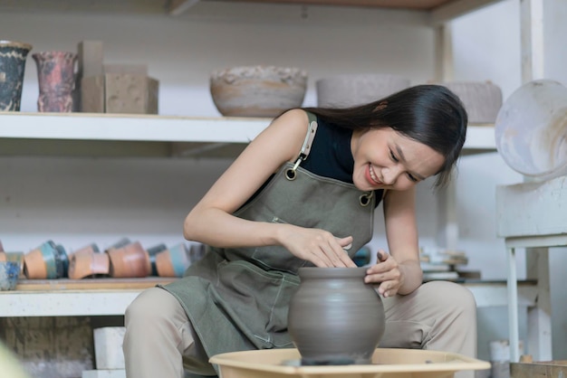 Primer plano de las manos femeninas que trabajan en alfareros rueda escultura femenina asiática mujer formando molde pequeño jarrón tazón de arcilla en la rueda de alfarero en casa estudio taller arte y creación hobby concepto