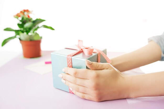 Primer plano de manos femeninas sosteniendo un regalo. El escritorio rosa de moda.