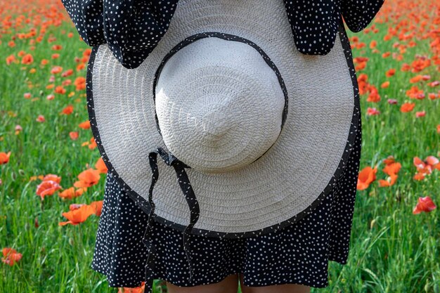 Primer plano de manos femeninas sosteniendo sombrero de verano el fondo del campo con concepto de vacaciones de amapolas