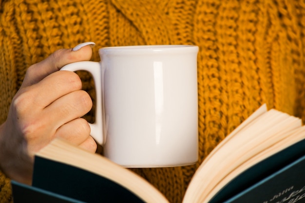 Primer plano de manos femeninas con una taza de bebida hermosa mujer en gritar suéter sosteniendo una taza de té