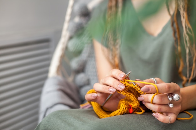 Primer plano de manos femeninas con tejido. Agujas de tejer de metal. Tejido de punto amarillo.