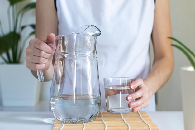 Primer plano de manos femeninas vertiendo agua potable en un ritual matutino de vidrio para la salud